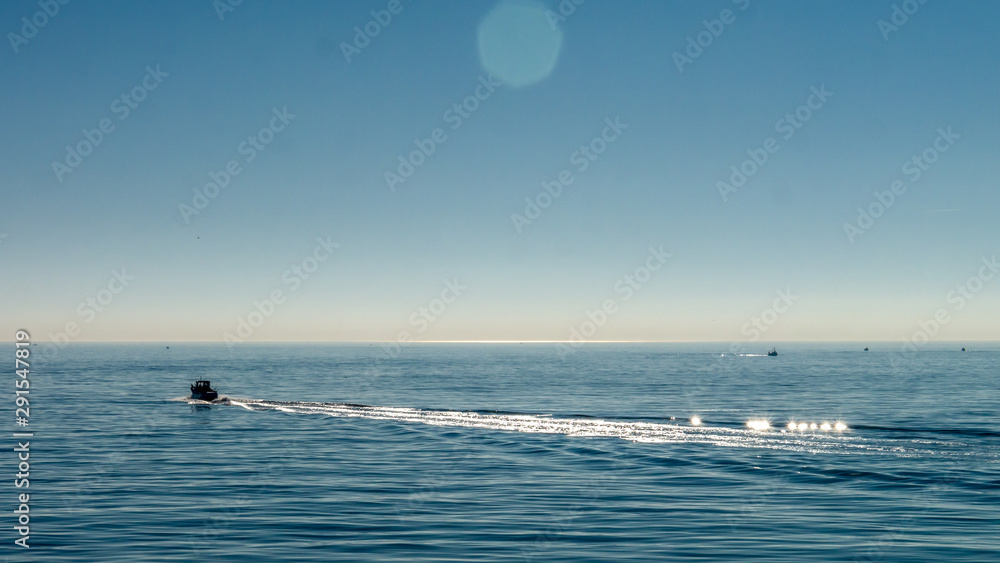 Small motor powered speed road creating waves in the North Sea, taken at Roker Pier, Sunderland, Tyne & Wear, England UK. Image with blue cloudless sky and calm, serene sea.