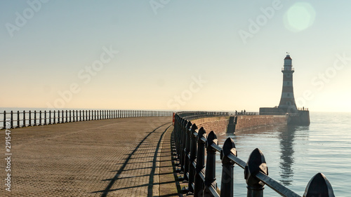 Roker Pier with black metal railing in Sunderland, Tyne and Wear, England UK.  With Roker Lighthouse in the background a cloudless sky, clam North Sea and warm sunshine. photo