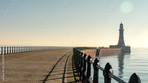 Roker Pier with black metal railing in Sunderland, Tyne and Wear, England UK.  With Roker Lighthouse in the background a cloudless sky, clam North Sea and warm sunshine.