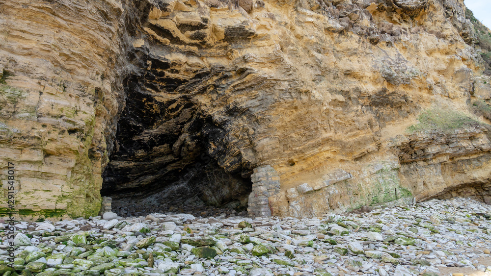 Natural cave embedded in a limestone rock, cliff face structure with a loose rock floor. Taken at Marsden Bay, South Shields, Tyne and Wear, England UK.