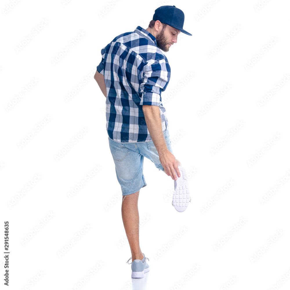 Man in jeans shorts, cap, casual clothing standing looking sole sneaker on white background isolation, rear view Man in jeans shorts, cap, casual clothing standing looking sole sneaker on white background isolation, rear view