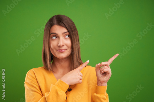 Close up of woman in yellow sweater thinking and pointing over green background