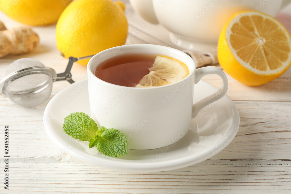 Cup of tea with lemon, mint, strainer, ginger and teapot on wooden background, close up Cup of tea with lemon, mint, strainer, ginger and teapot on wooden background, close up