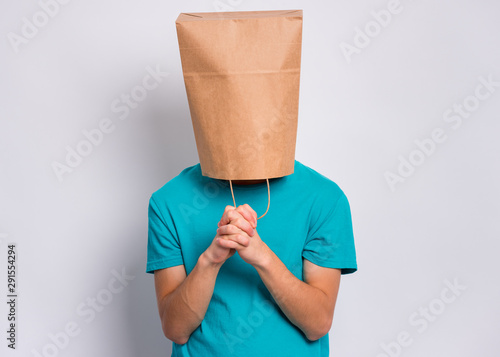 Teen boy with paper bag over head praying. Teenager cover head with bag  with hands folded in prayer hoping for better posing in studio. Child  asking God for good luck, success or
