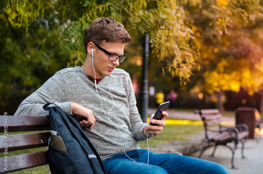Obraz premium Beautiful teen listening to music on park bench on beautiful autumn day 