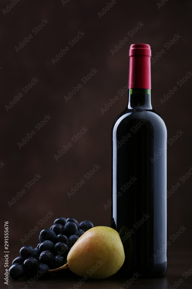 Fototapeta premium Bottle of wine with grapes and pear on brown background