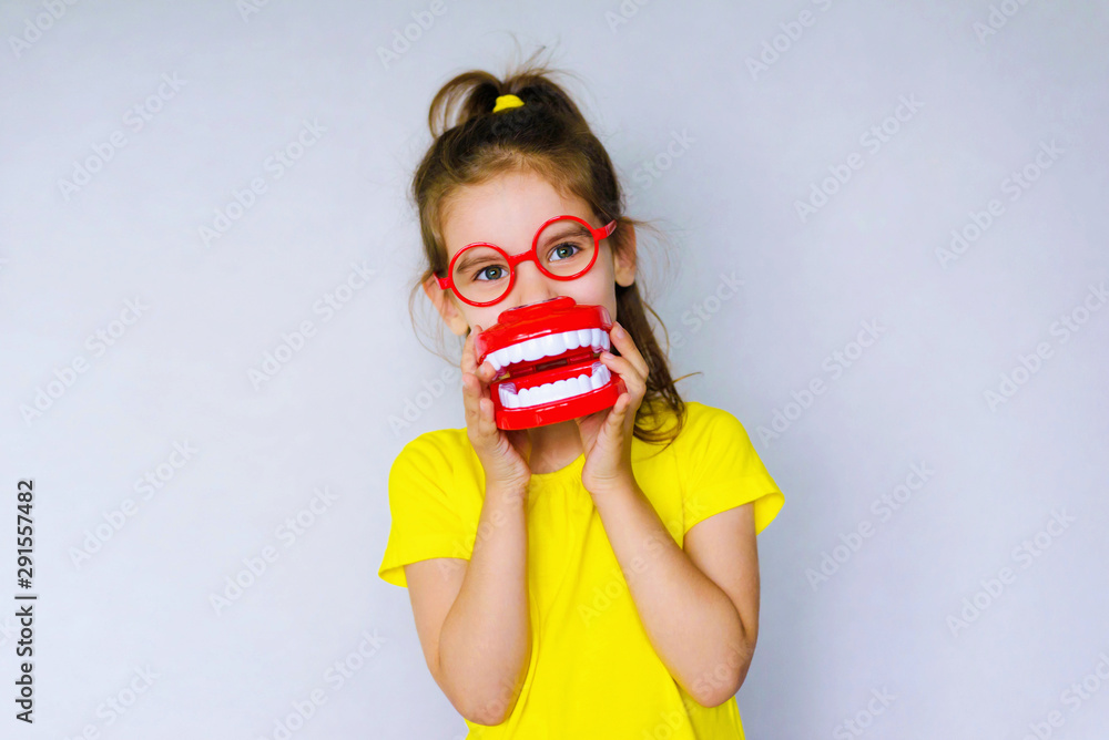 Little funny girl kid with toothbrush, dental mockup (jaw), red glasses in hand. Concept of health, oral hygiene, people and beauty. Space for your text. Selective focus. - obrazy, fototapety, plakaty 