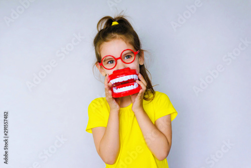 Little funny girl kid with toothbrush, dental mockup (jaw), red glasses in hand. Concept of health, oral hygiene, people and beauty. Space for your text. Selective focus. photo