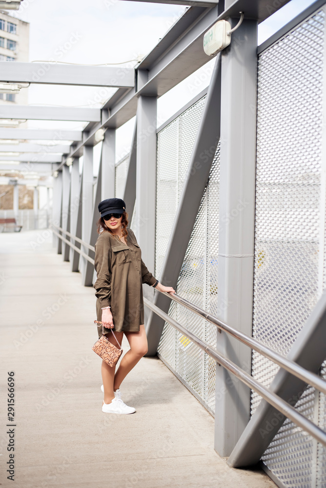 Fashion female model dressed casual in a grungy location. Fashion blogger in military shirt and hat on a pedestrian bridge