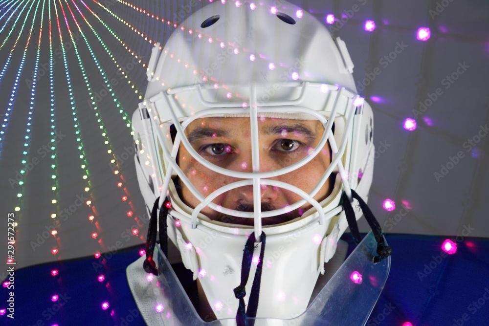 Detail of a male face in a white goalie hockey mask and colorful lights.This is a detail hockey goalie. He is concentrated on game. He has colorful lights under his eyes. Detail of a male face in a white goalie hockey mask and colorful lights.This is a detail hockey goalie. He is concentrated on game. He has colorful lights under his eyes.