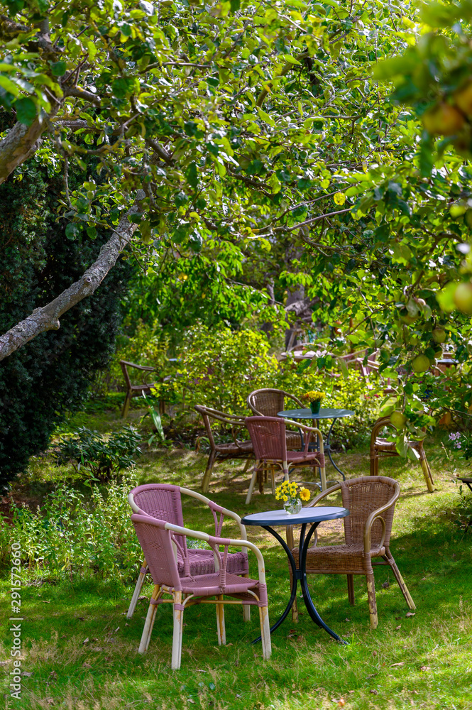 Cozy sitting areas made of wicker chairs and tables in a romantic orchard (format portrait). Cozy sitting areas made of wicker chairs and tables in a romantic orchard (format portrait).