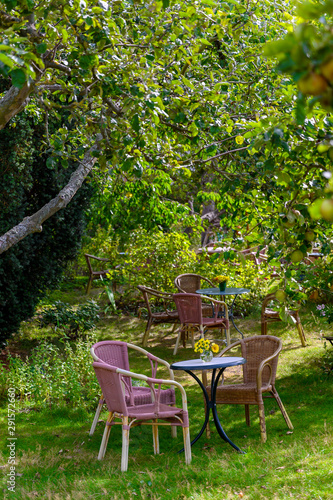 Cozy sitting areas made of wicker chairs and tables in a romantic orchard (format portrait).