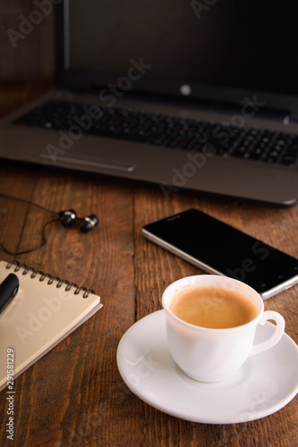 Cup of coffee on a laptop keyboard. Work place modern. Laptop  notebook  with cup of coffee and notepad with pen on old wooden table.