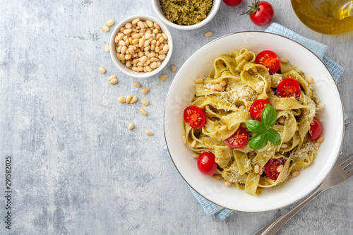 Fettuccine pasta with sauce pesto, cherry tomatoes, pine nuts and parmesan cheese on concrete background. Top view. Copy space.