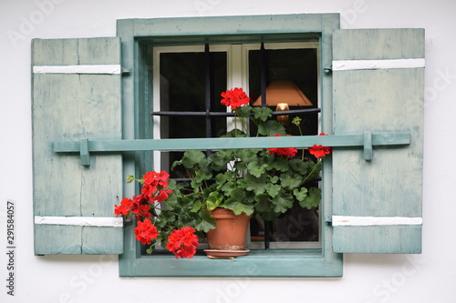 window of alpine house with wooden shutters and geranium flowers