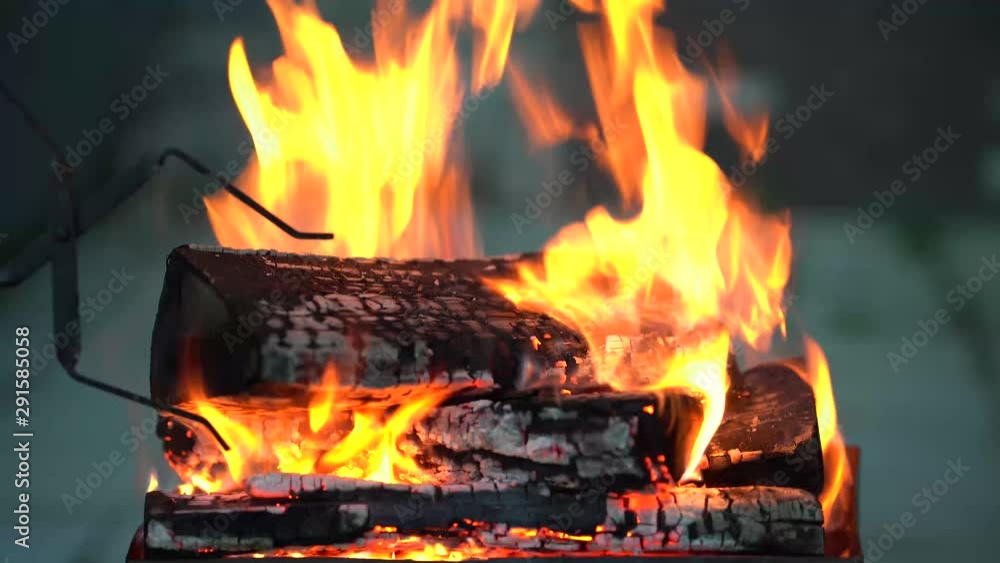 In the grill with a strongly burning wood man corrects tongs firewood and puts it in the fire new burning coals. In the grill with a strongly burning wood man corrects tongs firewood and puts it in the fire new burning coals.