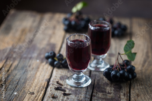 homemade black chokeberry wine or liqueur with ripe berries on wooden background
