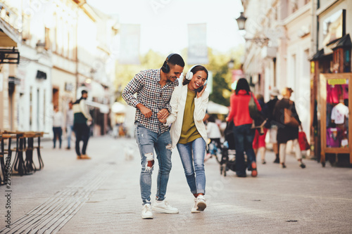 Happy young couple dancing on the street and listening to music through headphones
