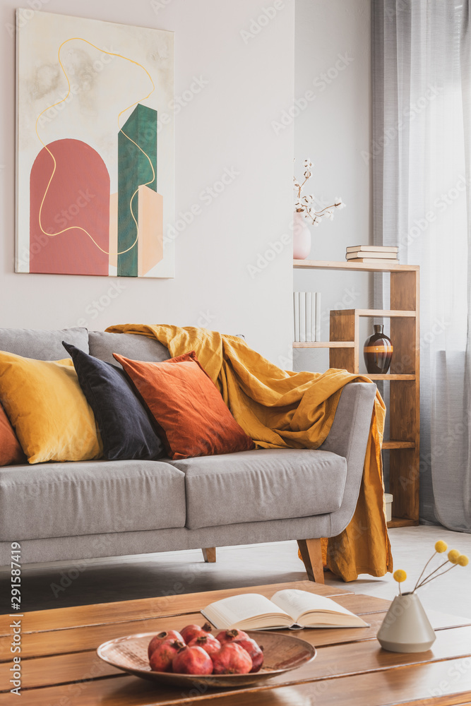 Yellow, orange, black and brown pillows on comfortable grey scandinavian  sofa in bright living room interior with abstract paintings on the wall  Stock Photo | Adobe Stock
