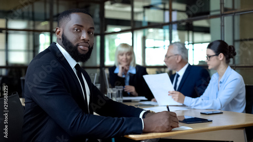 African office worker looking camera, business partners talking on background