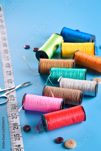 Sewing kit: scissors, measuring tape, thimbles, threads and buttons. Composition with threads and sewing accessories on blue background