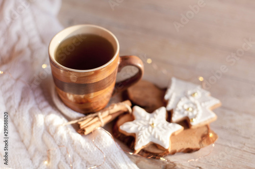 Christmas tea time. Mug of hot steamy beverage, gingerbread cookies at wooden and knitted background. Cozy morning breakfast with homemade sweets and cup. Winter food, drinks, new year lights.