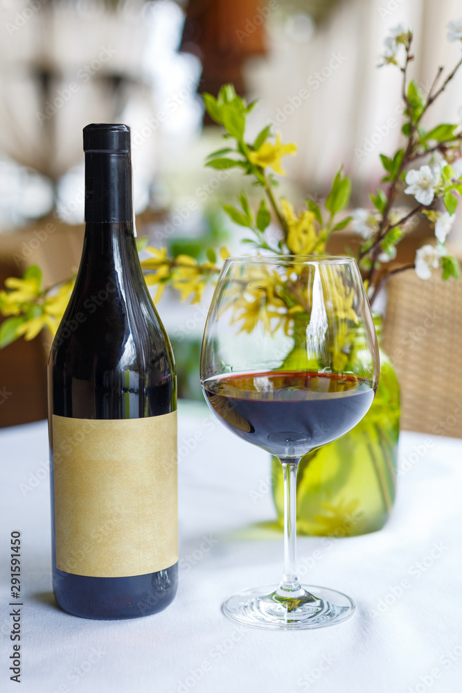 Bottle and glass of red wine on the table with spring decor. Restaurant table setting.