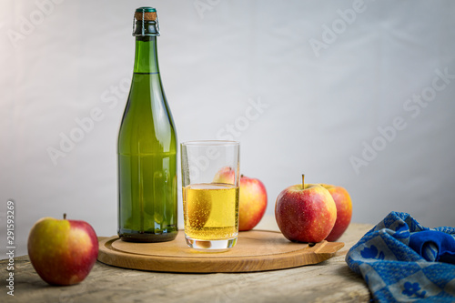 Apple cider in a glas with contextual elements, bottle, apples, tea towel, old plank