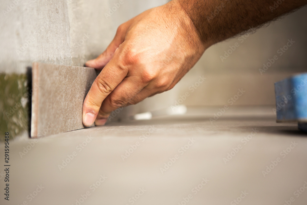 Hand of construction master gluing ceramic tile to wall.