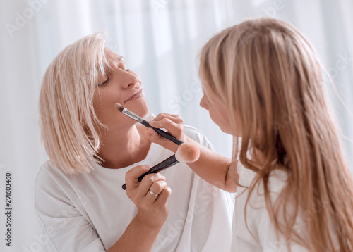 Mother and young daughter playing and applying make up together