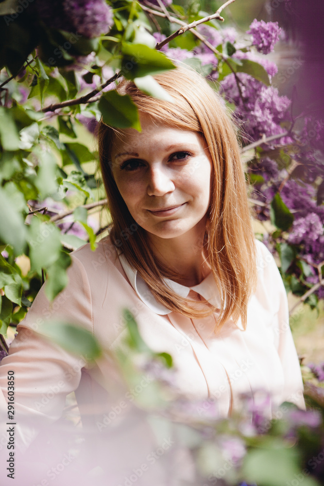 Fototapeta premium Beautiful young woman smiling with lilac flowers around in park