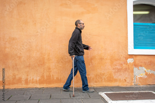Disabled man walks with walking stick and difficulty on the street