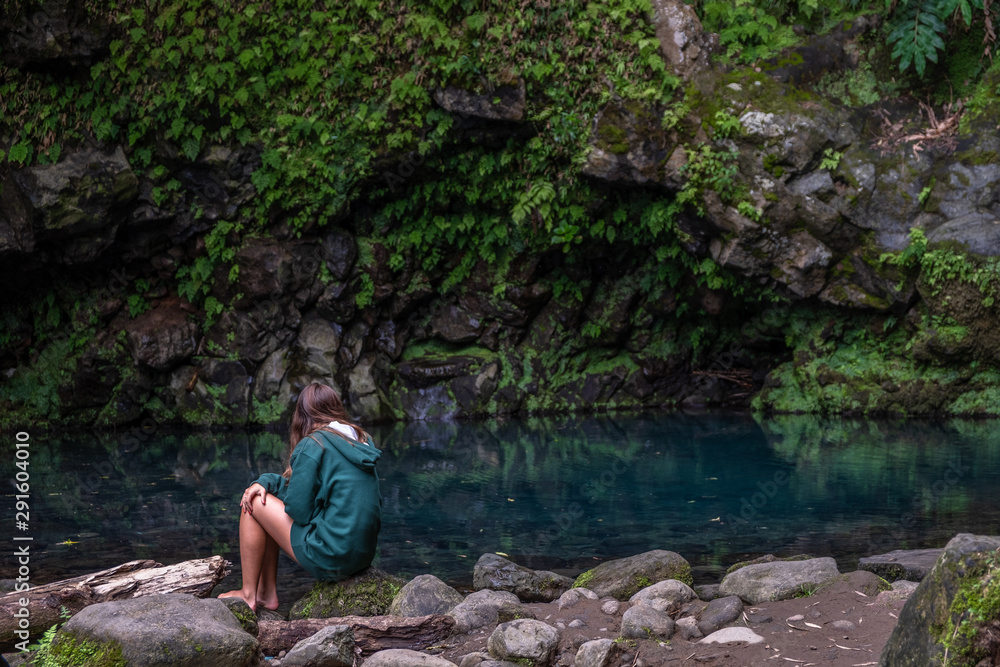 Young Girl contemplating Poco Azul waterfall (blue well) in a subtropical forest with blue color pool surrounded by green plants, Achadinha, Nordeste, São Miguel Island, Azores, Portugal