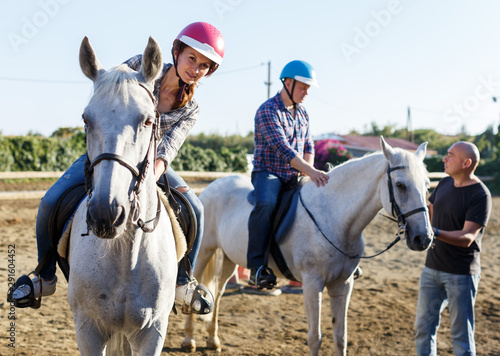 Mature couple with trainer riding horse at farm outdoor