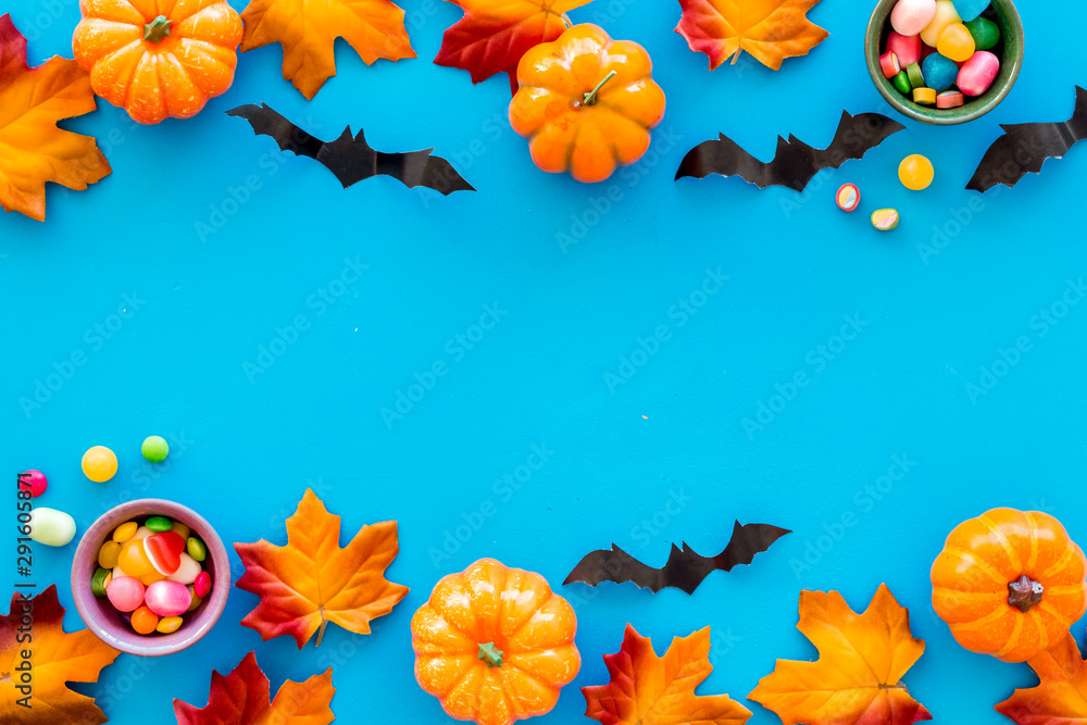 Bright Halloween composition with sweets, bats and pumpkins on blue background top view frame space for text Bright Halloween composition with sweets, bats and pumpkins on blue background top view frame space for text