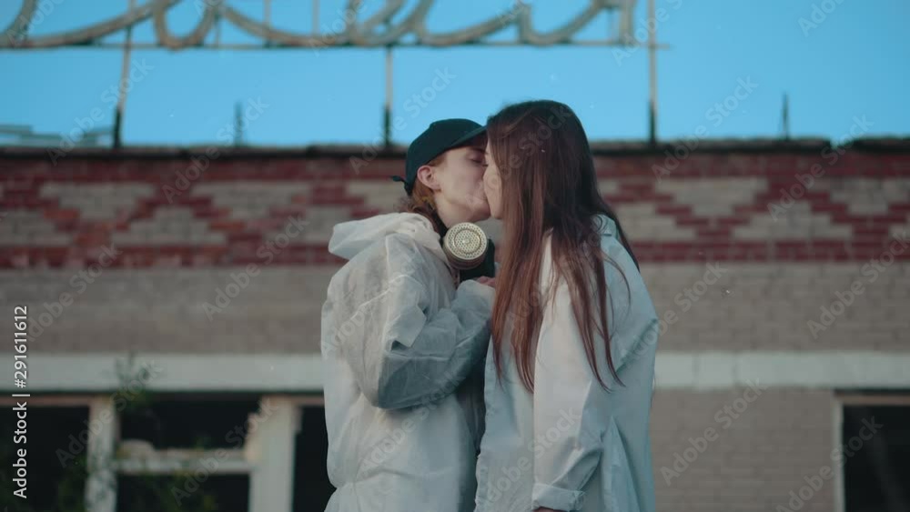 Two girls kiss on an abandoned territory. The lesbian was wearing protective masks. LGBT kiss. Protective suits from radiation. Lesbians kissing, gender equality. Stock ビデオ | Adobe Stock