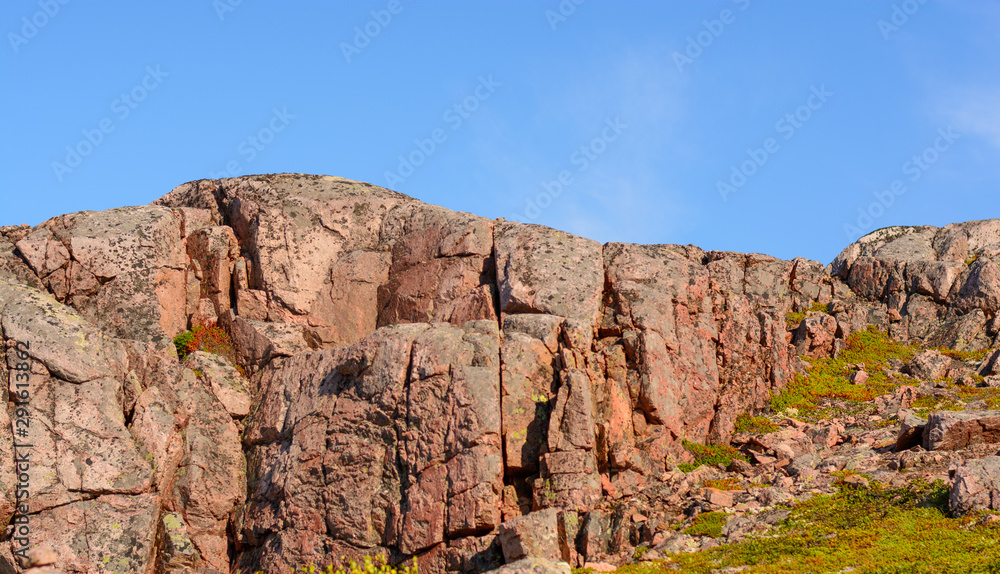 Pink colored mountain or hilltop surrounded by green grass and moss. Northern latitude is famous for its bright colors and low azure sky. Lots of stones on the upland.