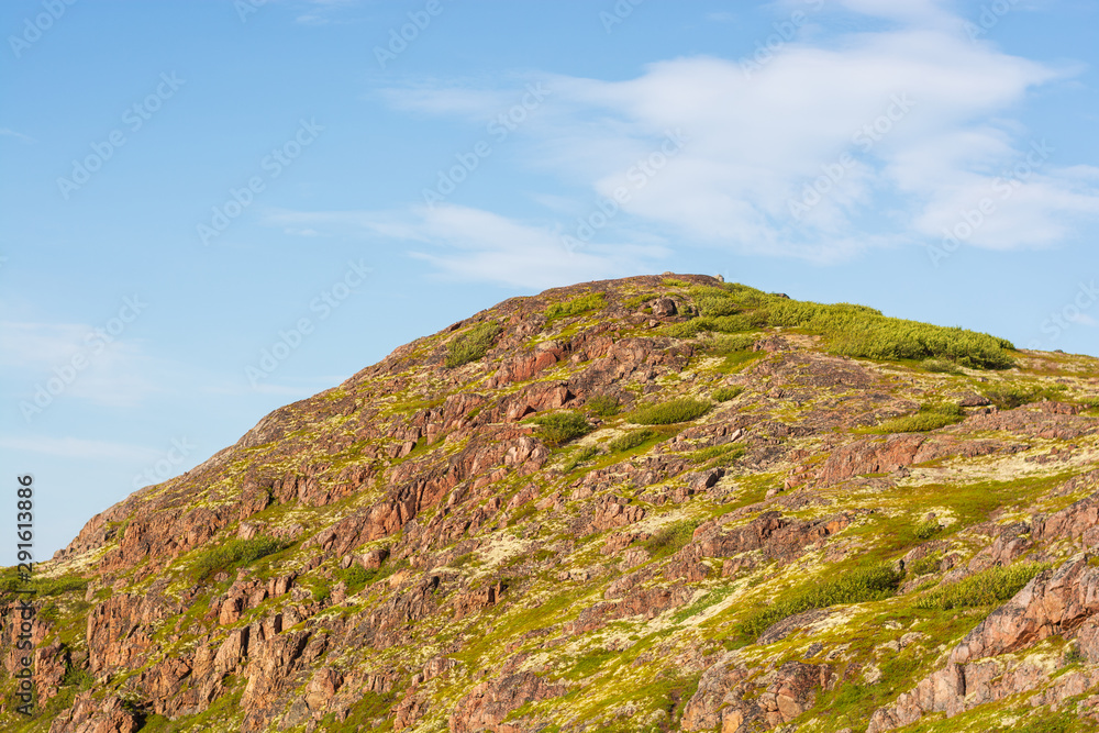 A gentle mountain on which grass and moss grow under a soft blue sky. Rock, dotted with winds and rains proudly rises.