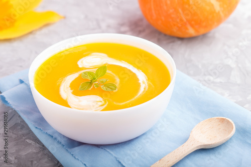 Traditional pumpkin cream soup with in white bowl on a gray concrete background with blue napkin. side view, selective focus.