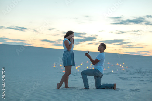 Fényképezés The guy makes the girl a marriage proposal by bending his knee while standing on the sand in the desert