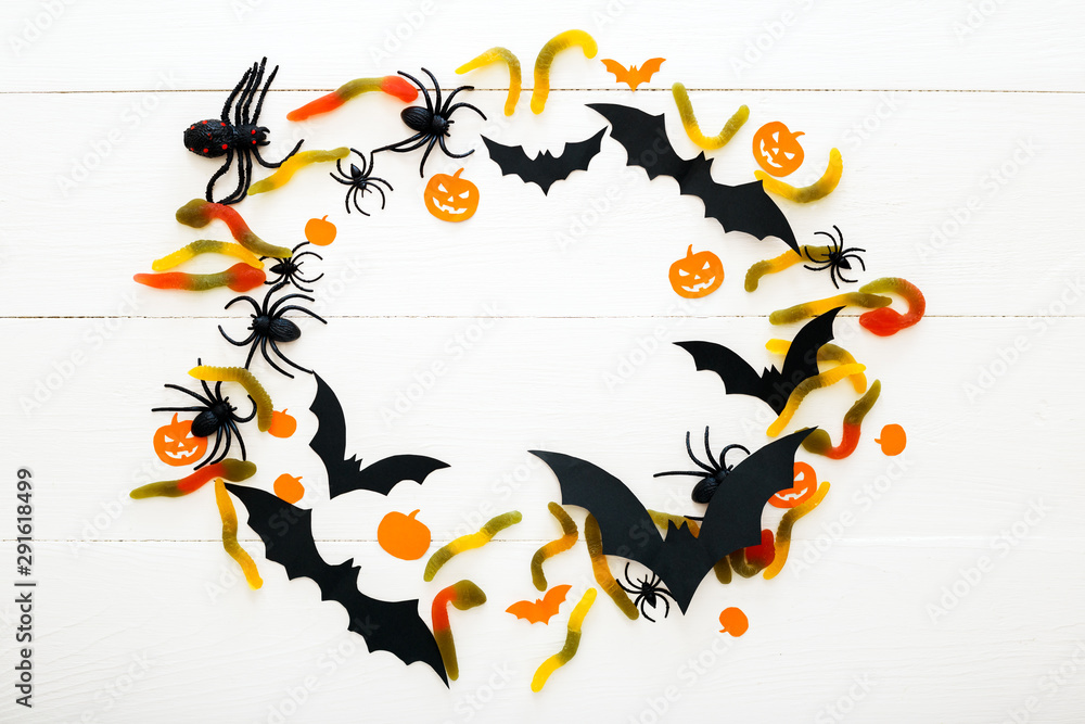 Halloween background with sweet candy, worms, paper bats, spiders, papar pumpkins on white wooden background. Halloween holiday decorations. Flat lay, top view, copy space. frame Halloween background with sweet candy, worms, paper bats, spiders, papar pumpkins on white wooden background. Halloween holiday decorations. Flat lay, top view, copy space. frame