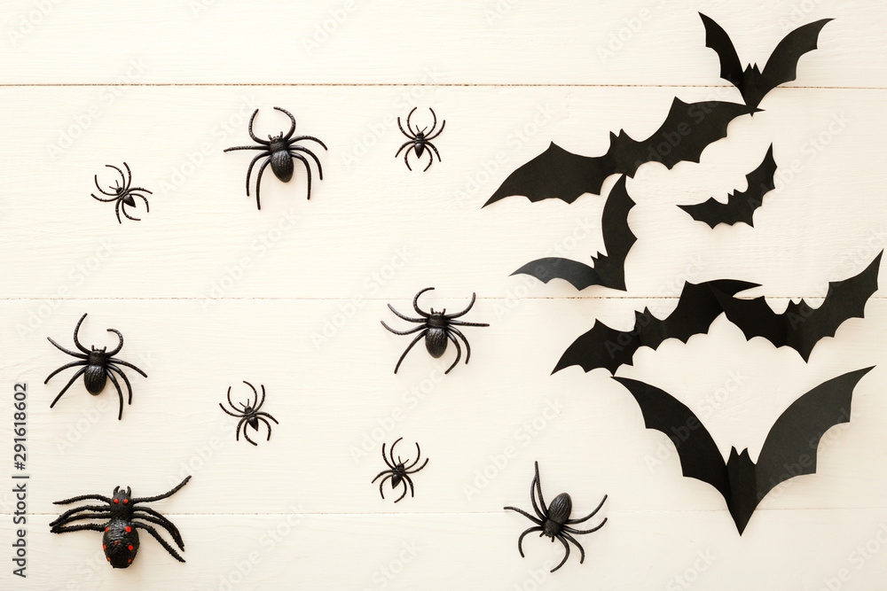 Halloween background with paper bats, spiders on white wooden background. Halloween holiday decorations. Flat lay, top view, copy space. Party invitation mockup, celebration.