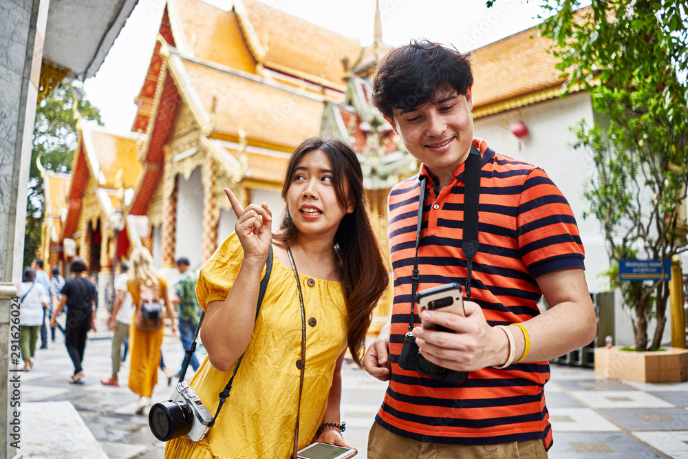 Obraz premium young thai couple looking at smartphone in front of Wat Phrathat Doi Suthep temple in chiang mai thailand