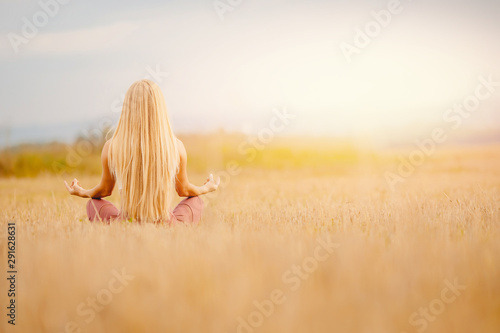 Back of girl blonde with long hair in lotus position meditates. Copy space