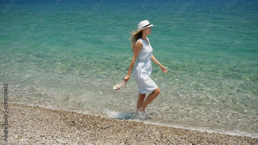 Young beautiful caucasian girl with white hat walks along the beach coastal view Young beautiful caucasian girl with white hat walks along the beach coastal view