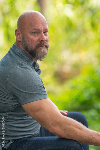 Fototapeta Naklejka Na Ścianę i Meble -  Man sitting outside looking towards camera. Man is in 50's with bald head and full beard