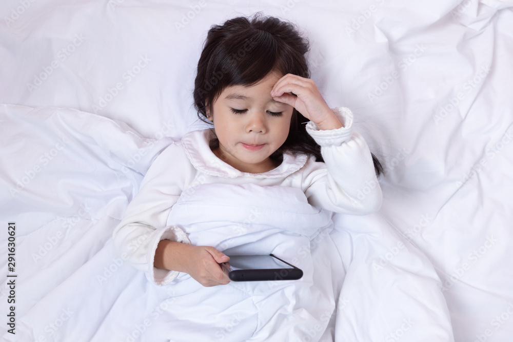 Little asian girl using smartphone and lying on the bed . child addicted phone.