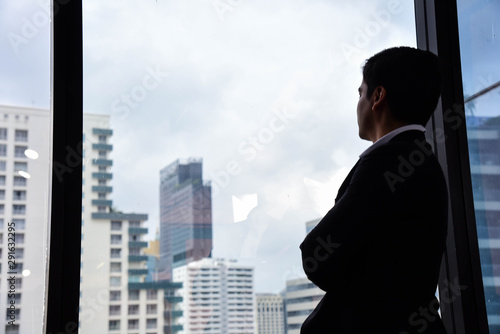 A handsome businessman look out of his office window on the tall building and think about the company development and new project in the future/Vision/Business going forward