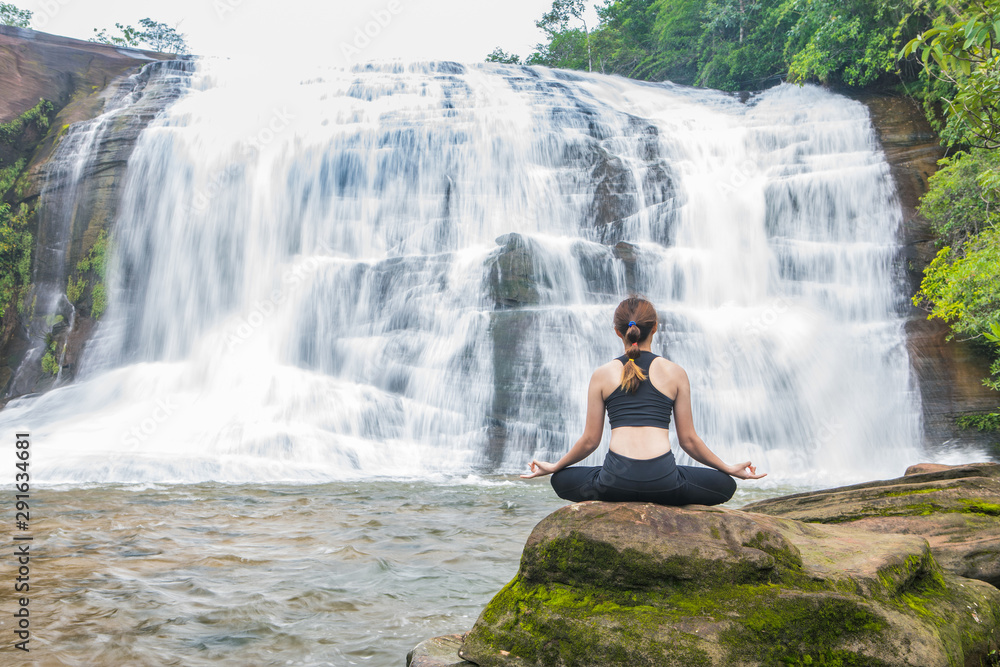 Young asain women practicing yoga at front of grand waterfall. Young asain women practicing yoga at front of grand waterfall.
