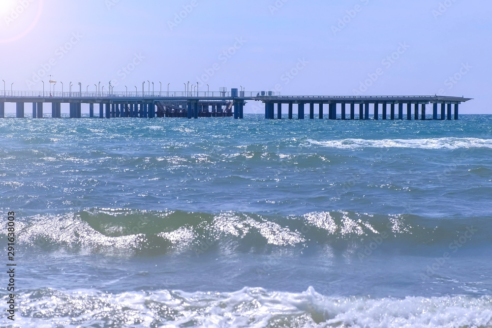 Helicopter platform and big pier at sea and stormy sea waves at windy day. Beautiful sea ocean background. Nature seascape with long waves, sky and pier at sunny day.